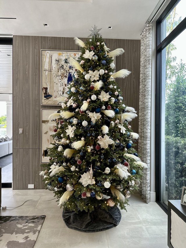 A slim tree in white and gold beside a glass door