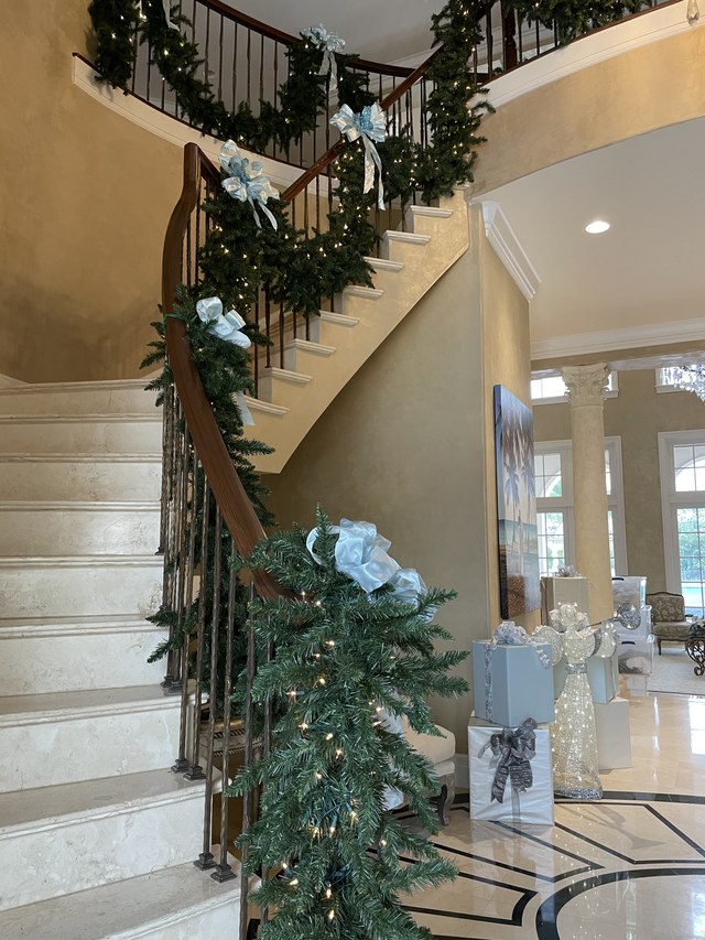 A curved staircase wrapped in greenery with white bows and ribbon