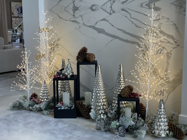 Lit birch trees, silver cones and pinecones against a marble wall