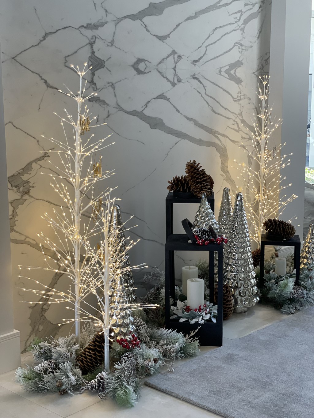 Lit birch trees and mercury glass cones against a marble wall