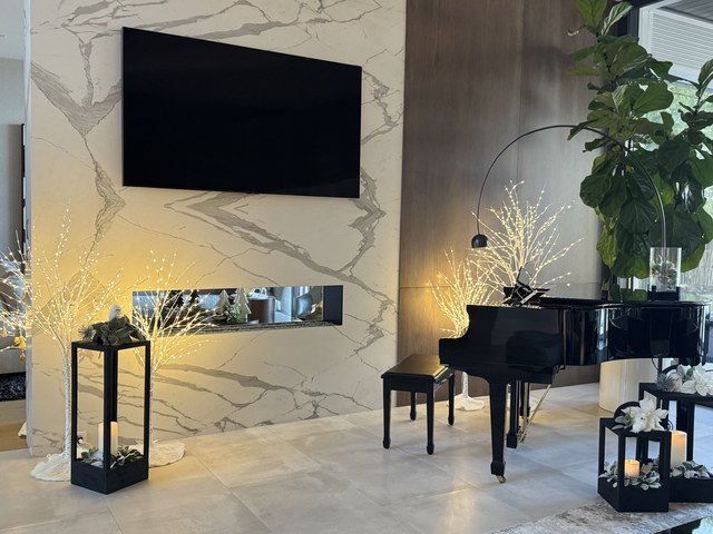 A marble fireplace wall with lit branches and lanterns beside a grand piano