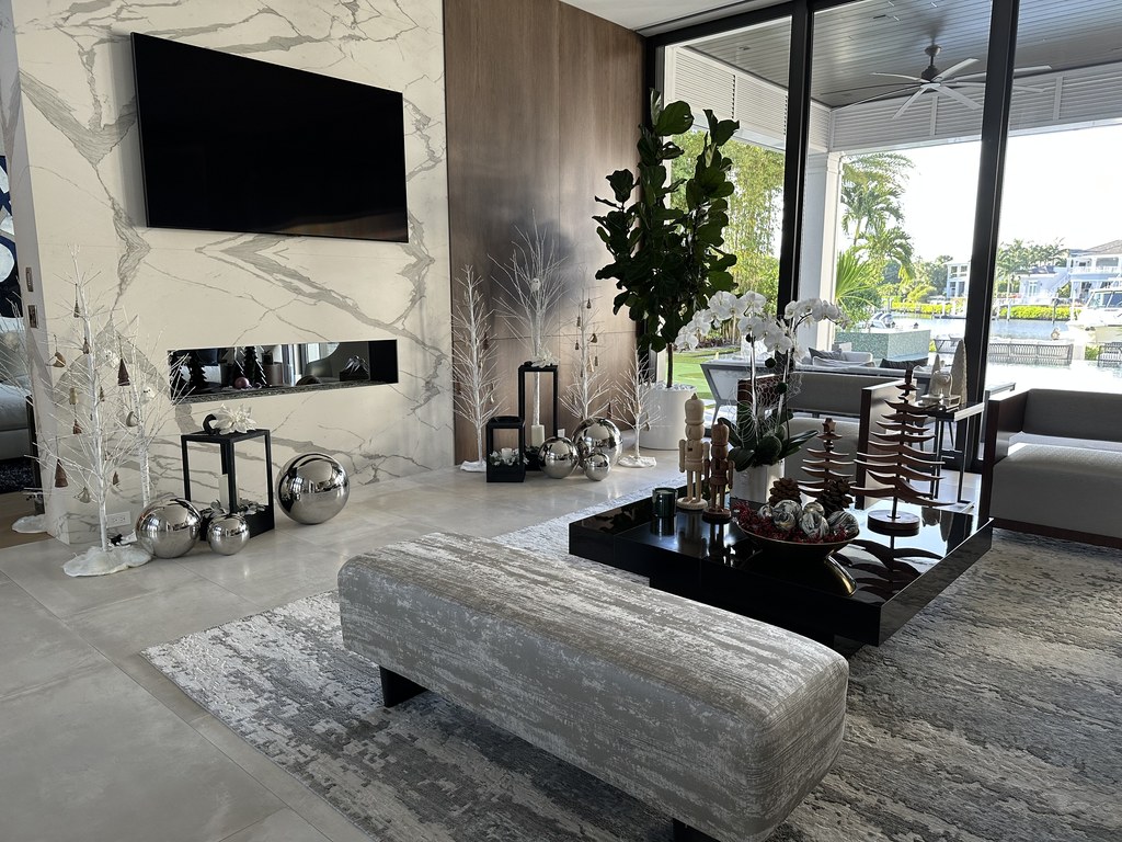 A living room with silver trees and mercury glass spheres on the marble fireplace wall, opening to the water