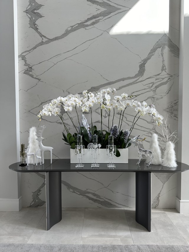 A console with white orchids and small white trees against marble