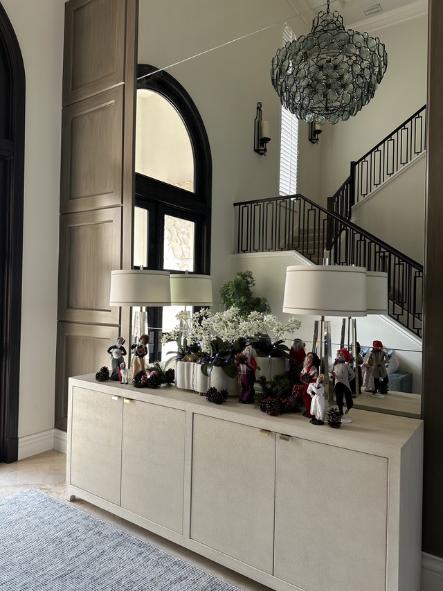 An entry console with white florals, paired lamps and a row of small figures