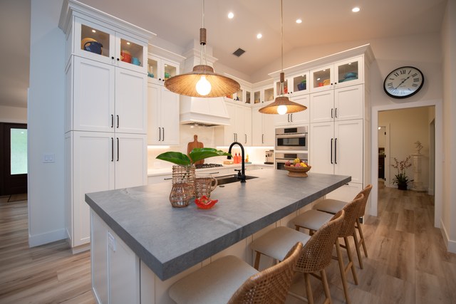 A white kitchen with a grey quartz island and woven counter stools