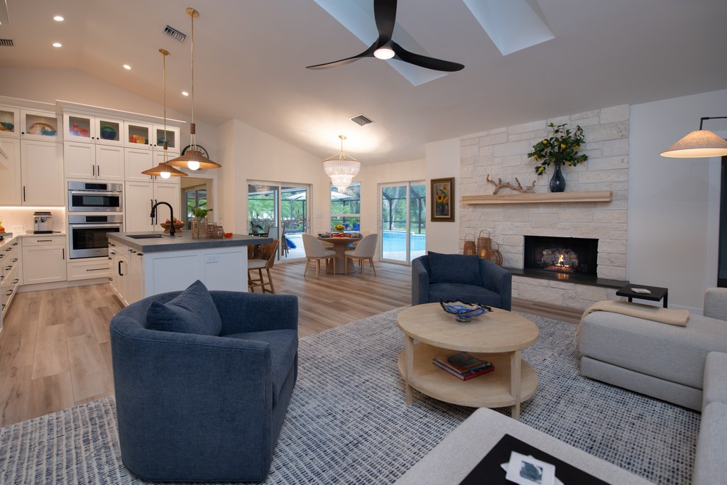 An open plan kitchen and family room with blue swivel chairs and a stone fireplace