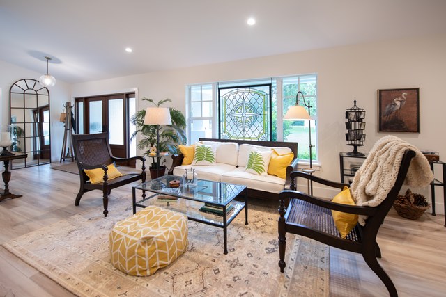 A formal living room with caned armchairs and a yellow ottoman