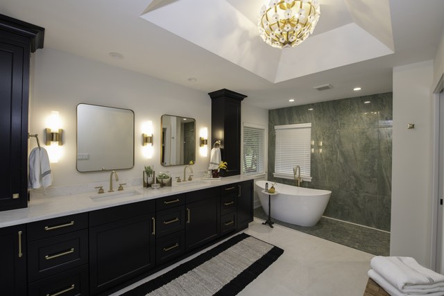 A primary bath with black double vanities, a soaking tub and green marble