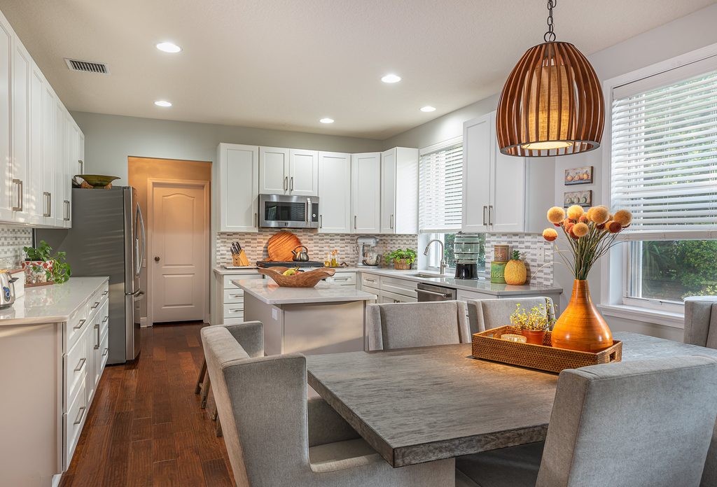 A white kitchen with a mosaic tile backsplash, a woven pendant and a concrete dining table
